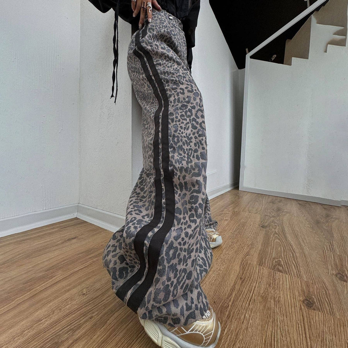 Person wearing leopard print pants with black stripes indoors on a wooden floor.