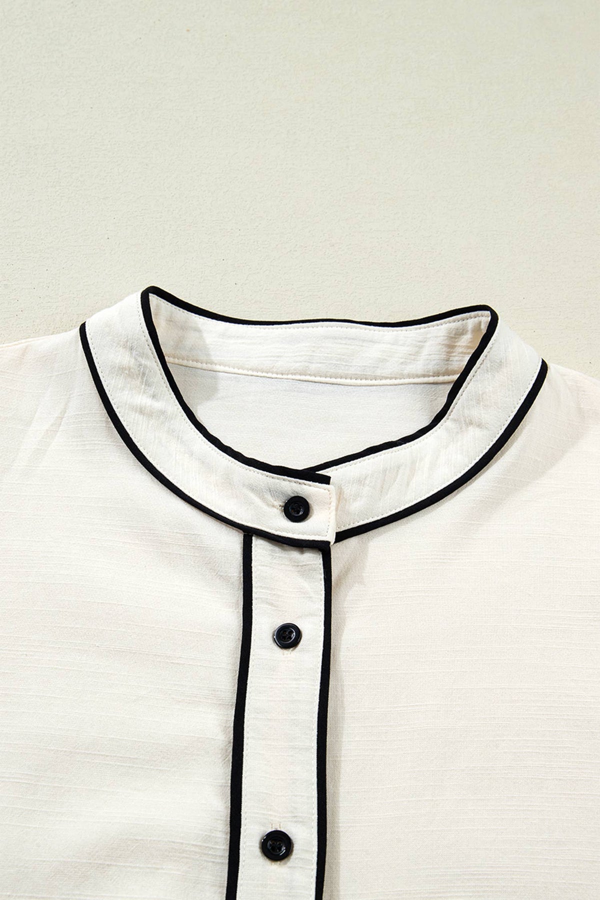 Close-up of a white shirt with black trim and buttons on a light background