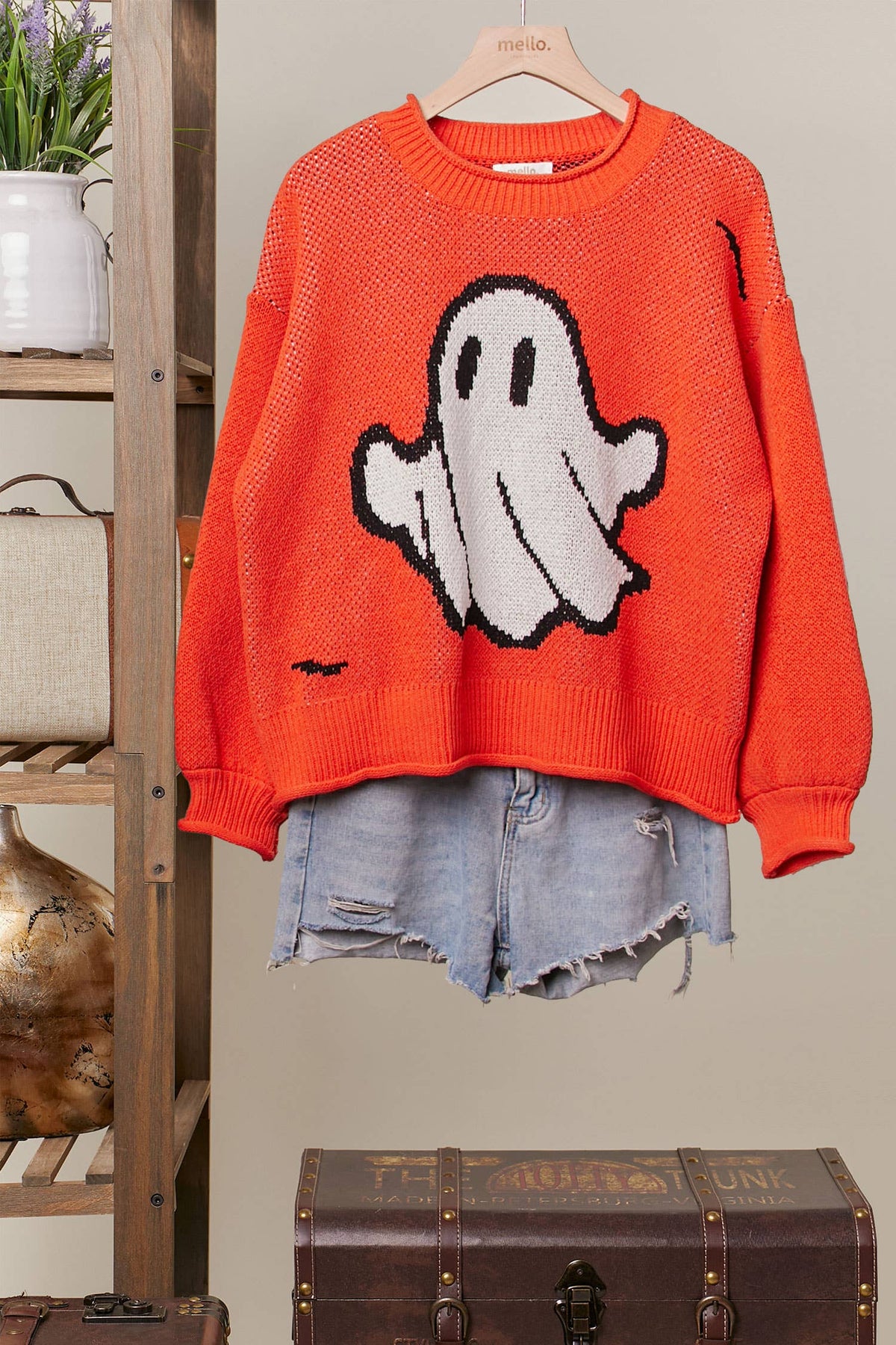 Orange sweater with ghost design on a hanger against a neutral background