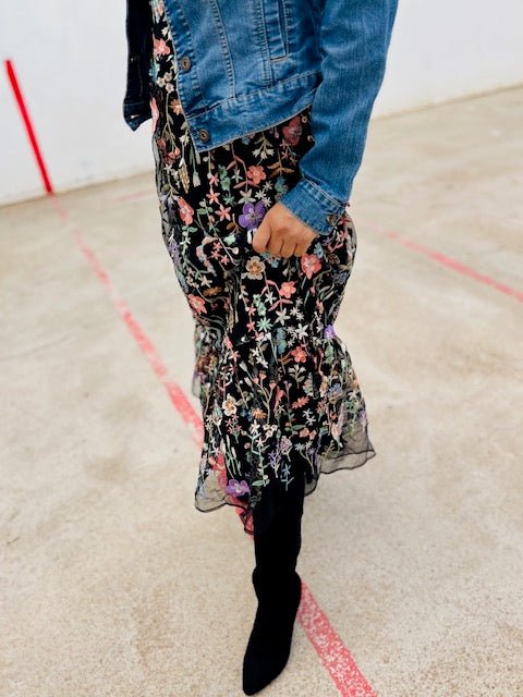 Person wearing a floral dress, denim jacket, and black boots on a plain background
