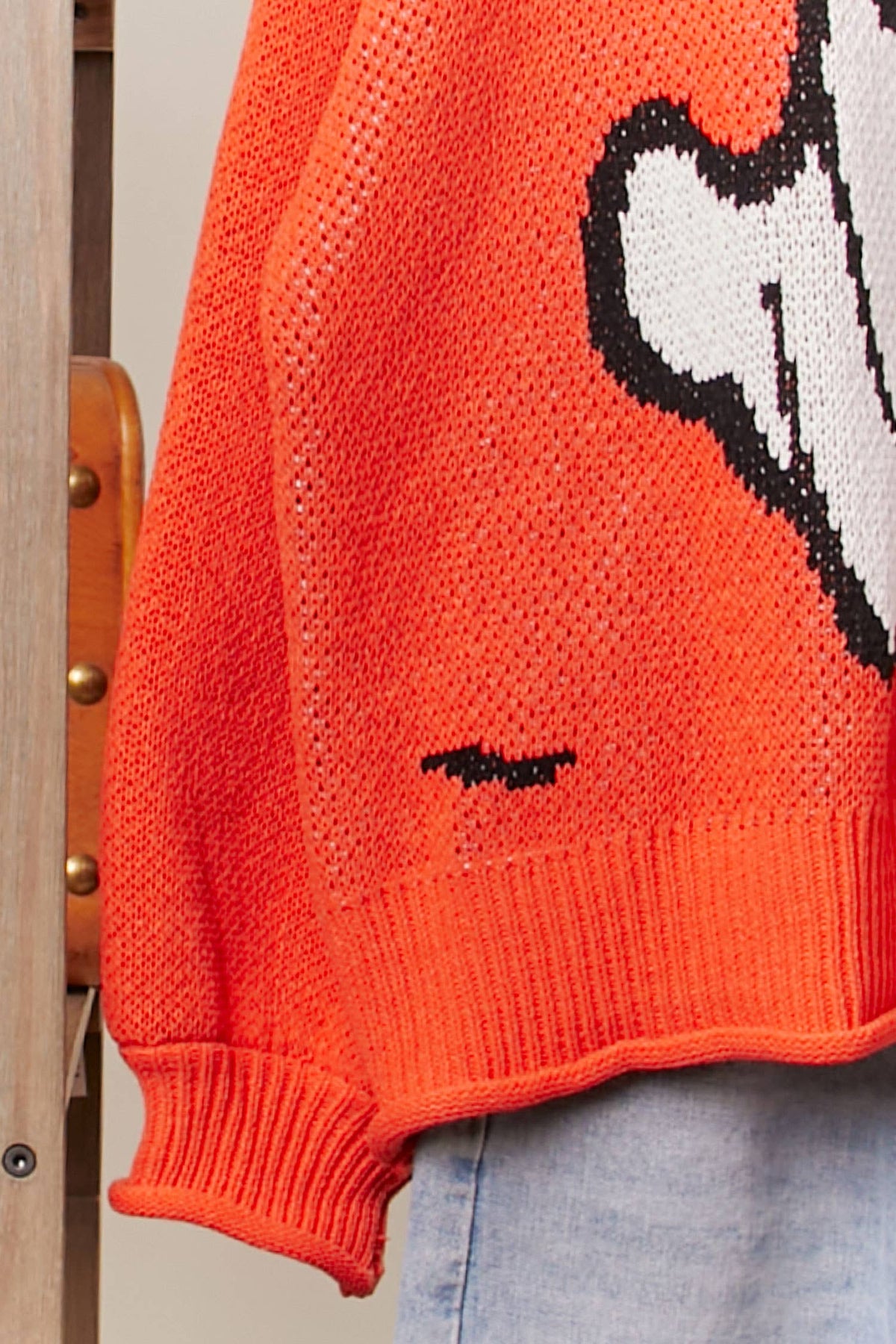 Close-up of an orange sweater with a graphic design on a wooden chair.