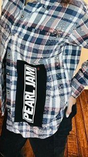 Person wearing a plaid shirt with a visible Pearl Jam band logo on a wooden floor.