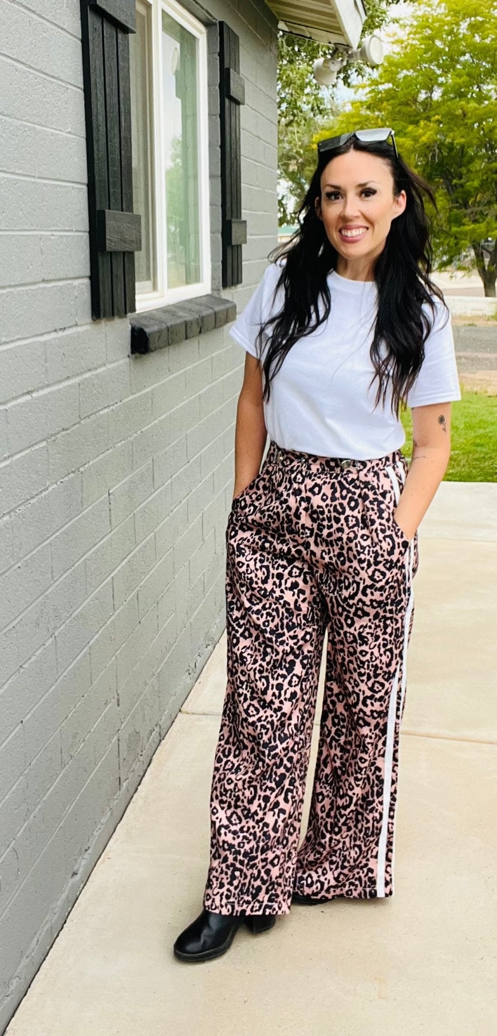 Woman wearing a white t-shirt and leopard print pants standing outside a house.