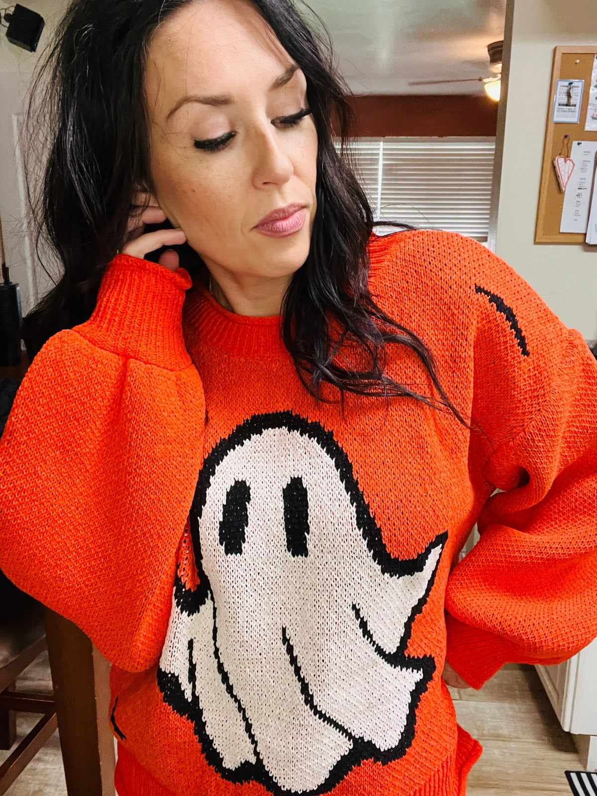Person wearing an orange sweater with a ghost design indoors.