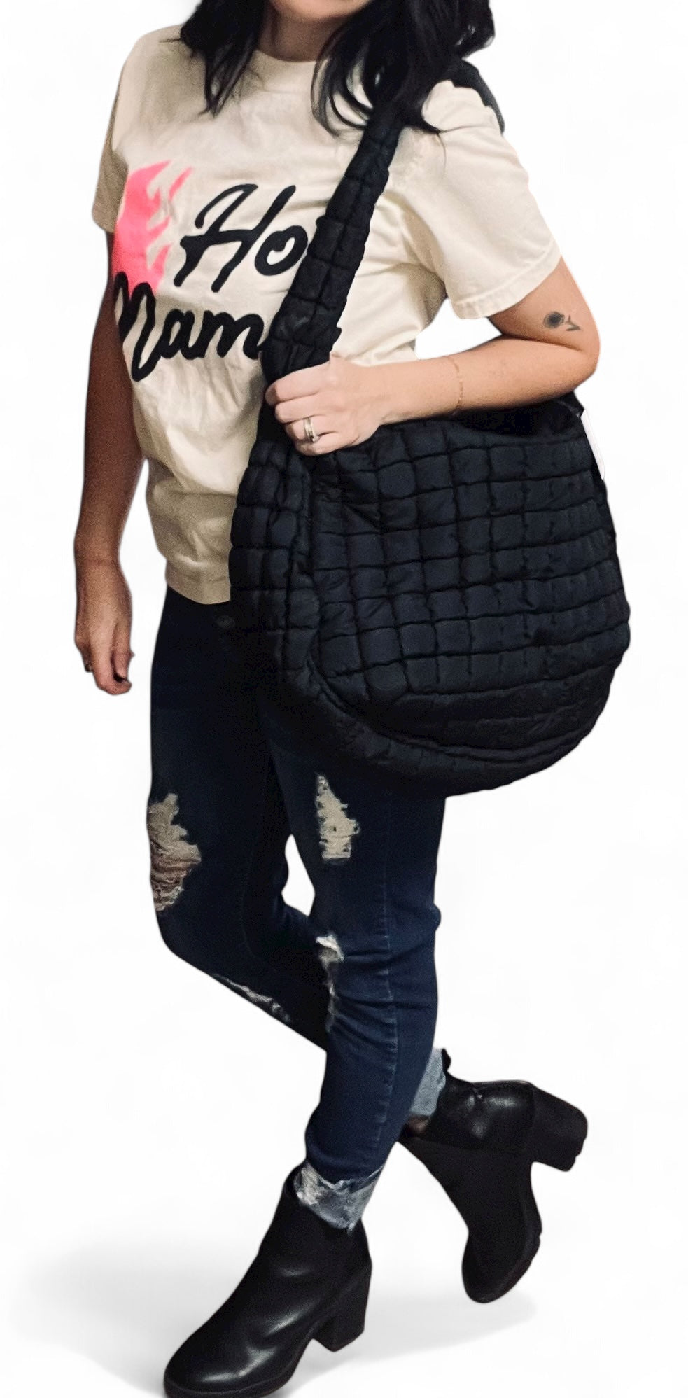 Person wearing a beige t-shirt with text, dark jeans, and black boots, carrying a black quilted bag.