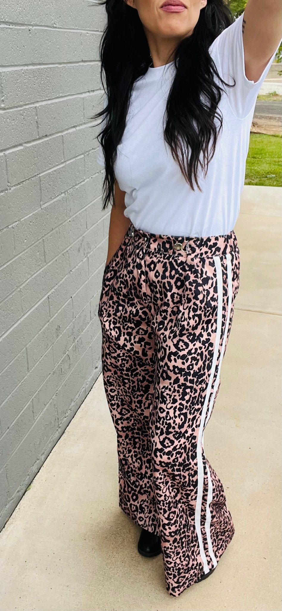 Person wearing a white t-shirt and leopard print pants with white stripes outdoors.