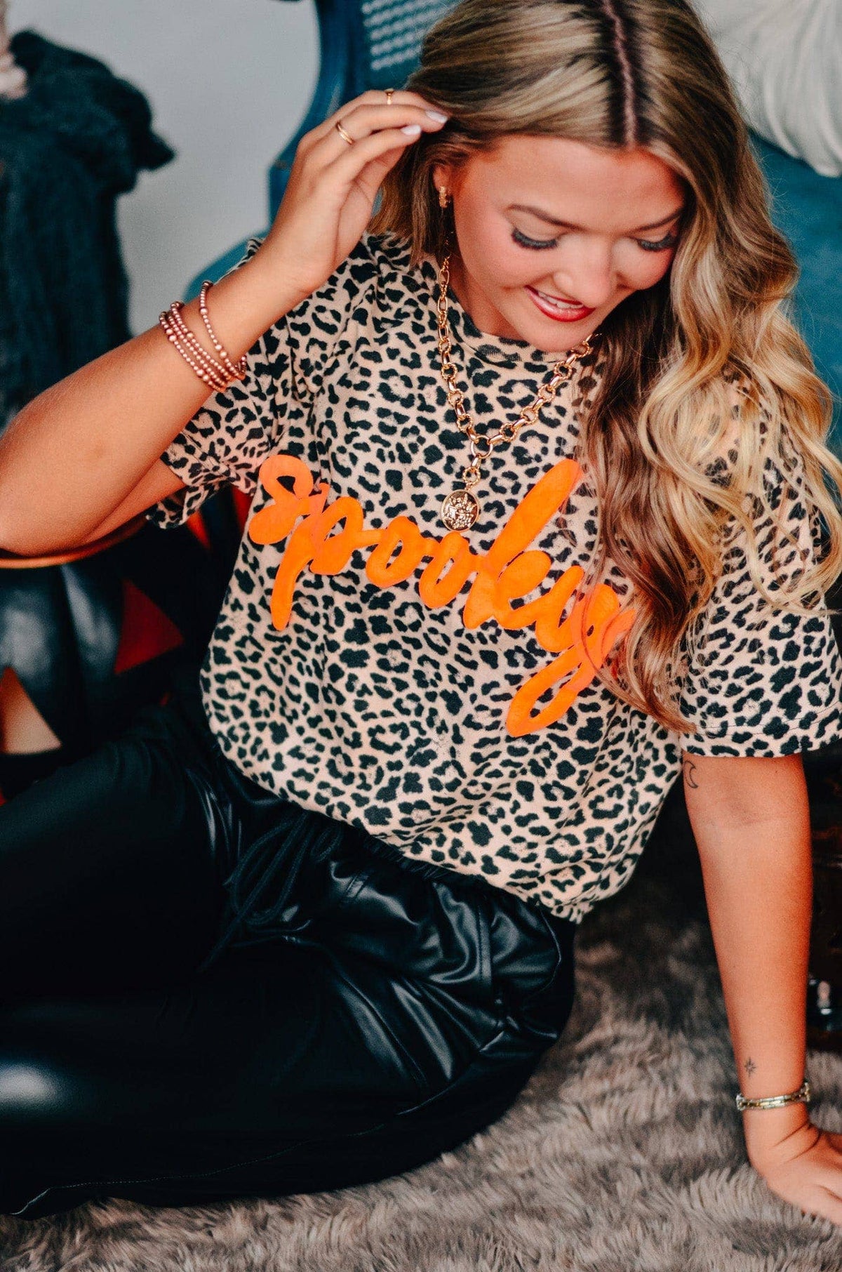 Woman wearing a leopard print shirt with 'Spooky' text, sitting on a carpeted floor.