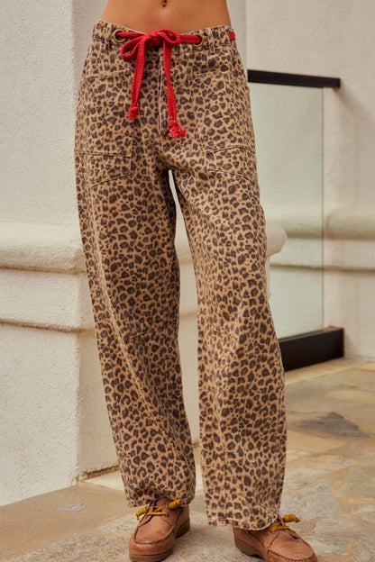 Leopard print pants with a red drawstring worn by a person, standing against a neutral background.