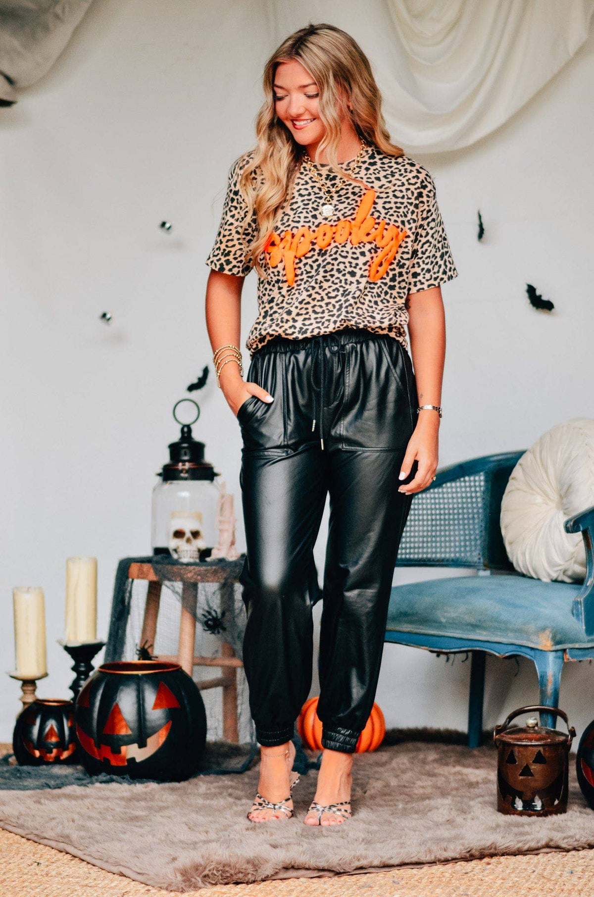 Woman in leopard print top and black pants standing in a room with Halloween decorations.