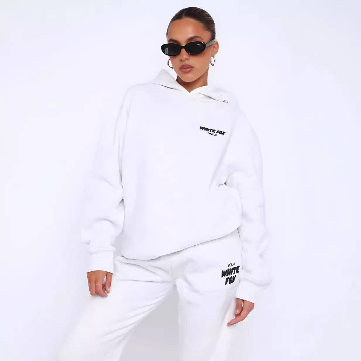Person wearing a white hoodie and pants with text, standing against a white background