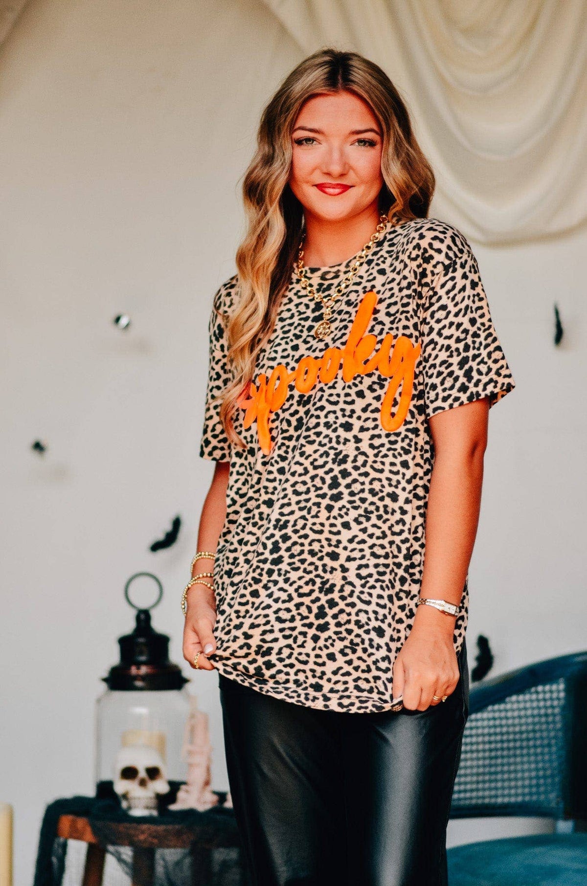Woman wearing a leopard print shirt with orange text in a Halloween-themed room.