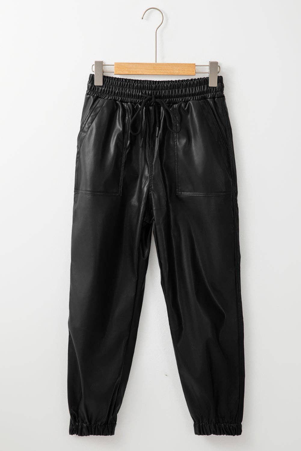 Black leather jogger pants on a hanger against a white background