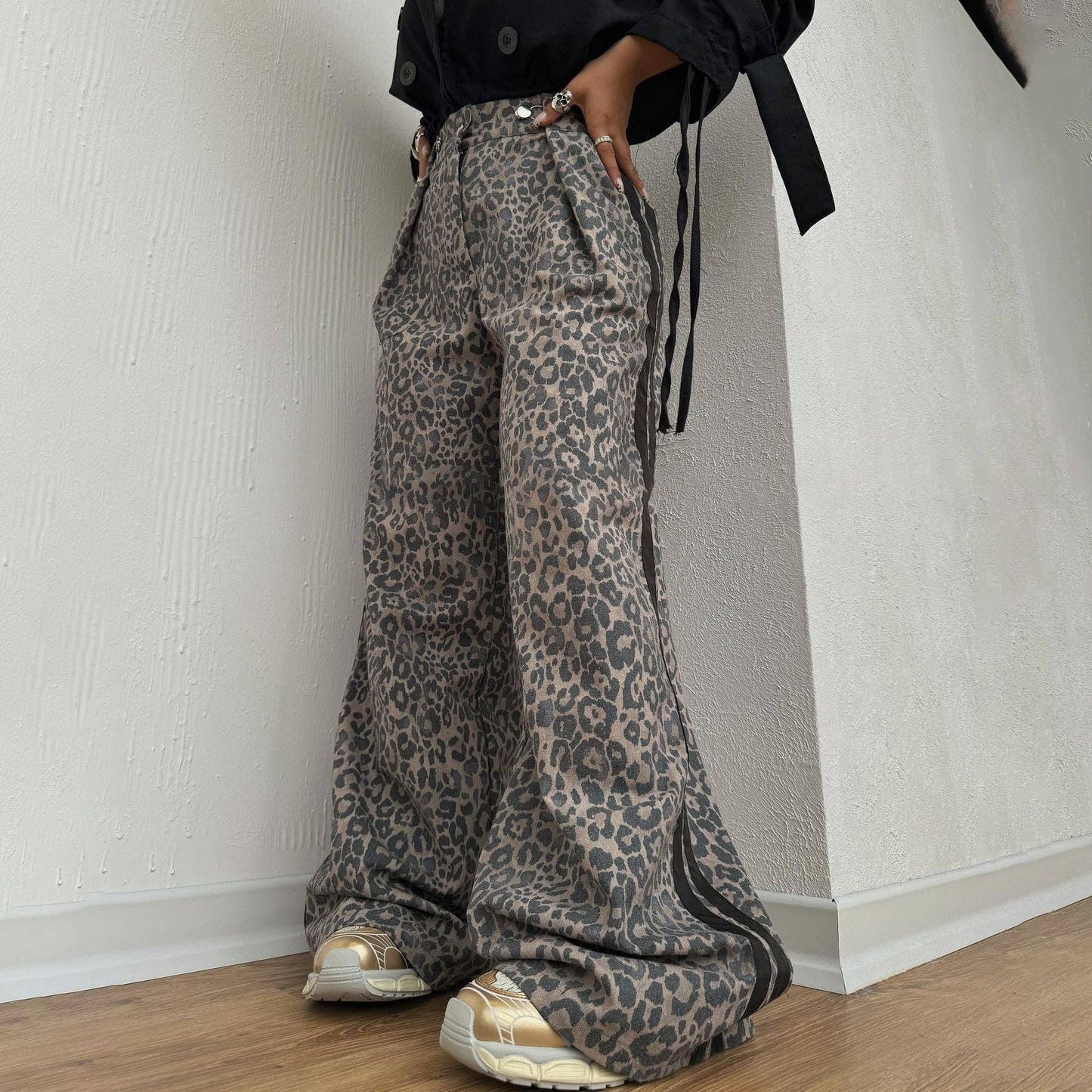 Person wearing leopard print pants and black jacket against a white wall.