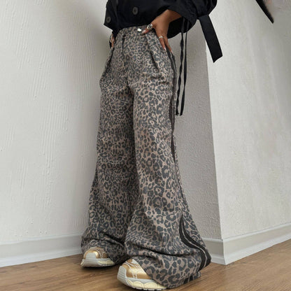 Person wearing leopard print pants and black jacket against a white wall.
