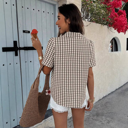 Woman in a checkered shirt and shorts eating ice cream, standing in front of a white door with a blue frame.