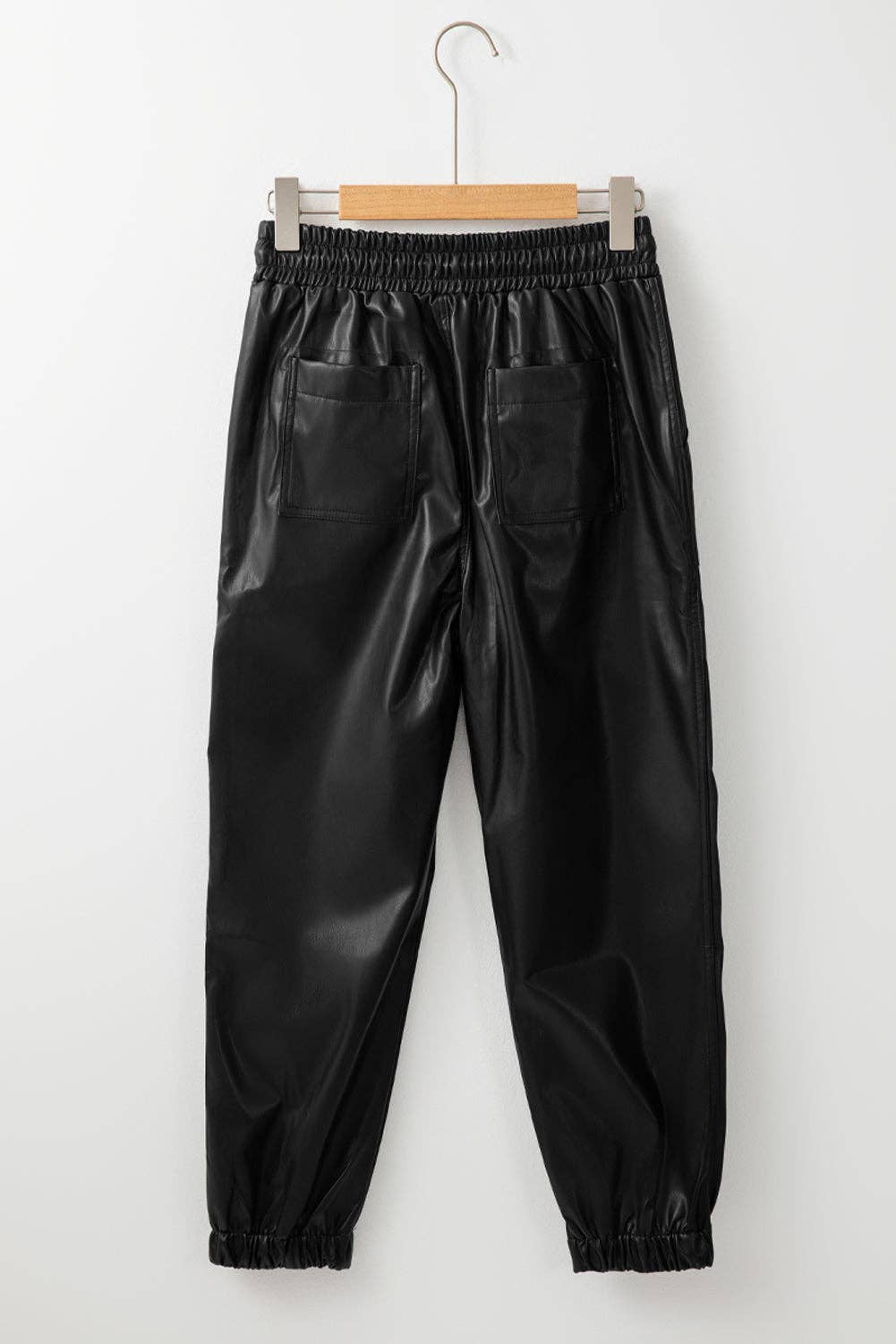 Black leather pants on a hanger against a white background