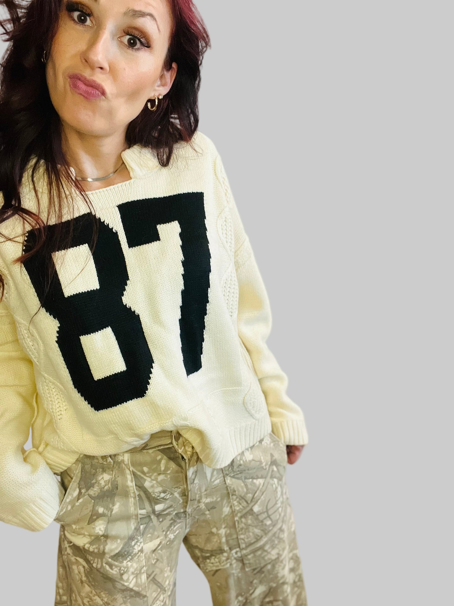 women in camo pants and 87 sweater in front of the white backdrop