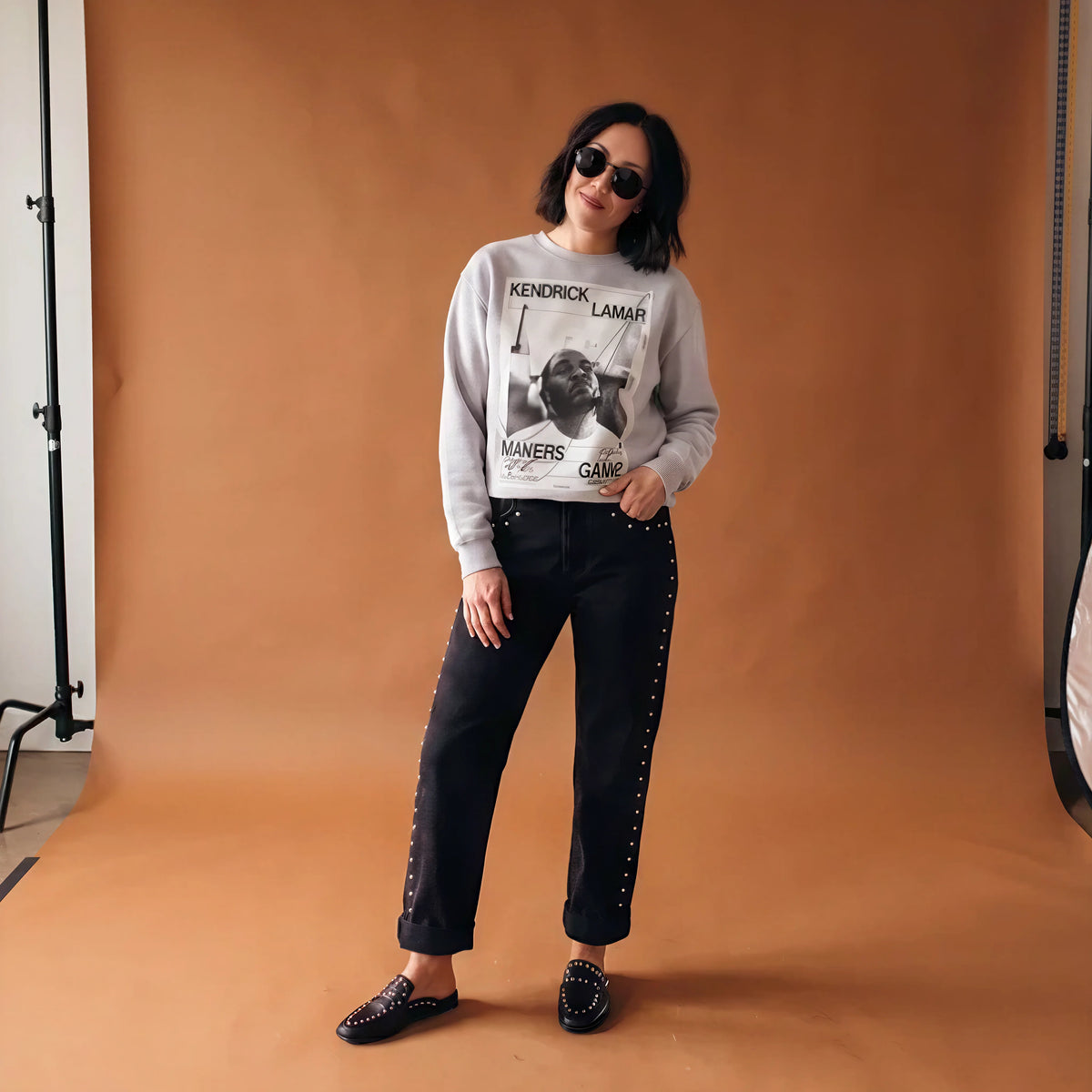 orange background with woman in kendrick lamar sweater with black pants and black loafers