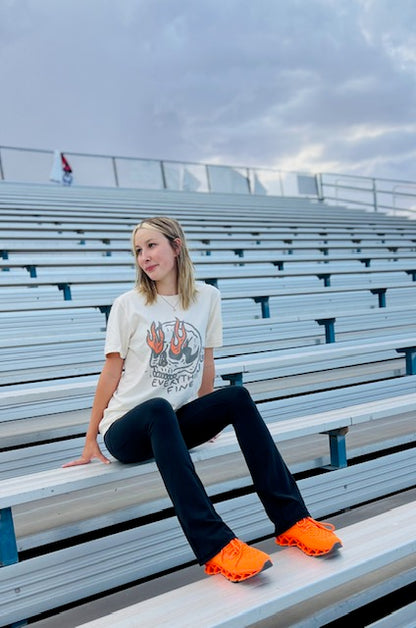 Person sitting on bleachers wearing a graphic t-shirt and bright orange shoes.