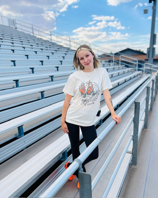 Person standing on bleachers with a white t-shirt featuring a graphic design.