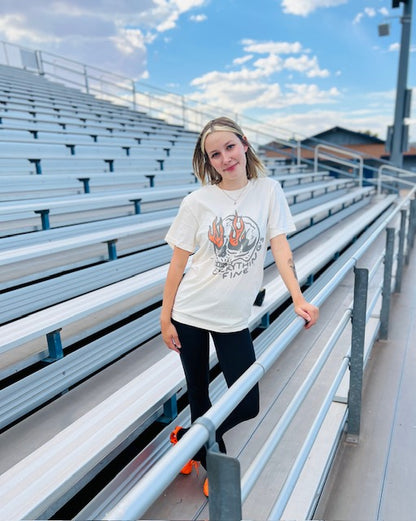Person standing on bleachers with a white t-shirt featuring a graphic design.