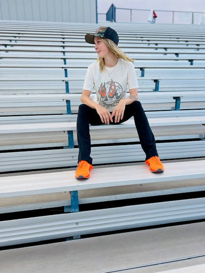 Person sitting on bleachers wearing a graphic t-shirt, black pants, and orange shoes.