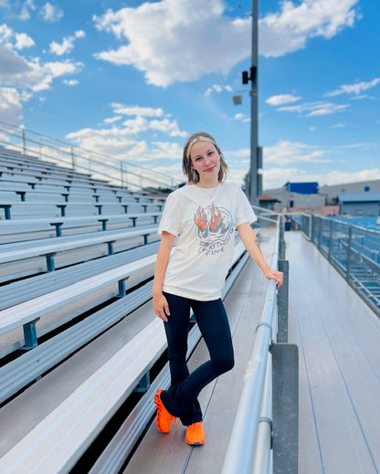 Person standing on bleachers with a white t-shirt and orange shoes, blue sky in the background
