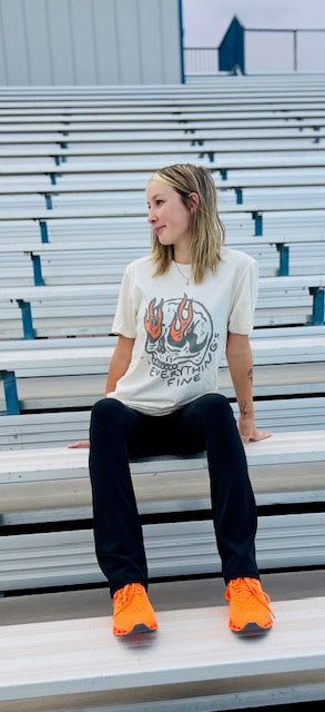 Person sitting on bleachers wearing a graphic t-shirt and bright orange shoes.