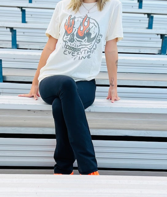 Person wearing a graphic t-shirt and dark pants sitting on bleachers.