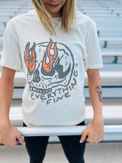 Person wearing a white t-shirt with a skull design and text, standing against a metal bleacher background.