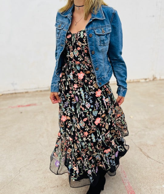 Person wearing a floral dress with a denim jacket against a plain background