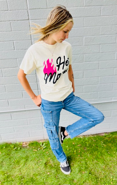 Person wearing a white t-shirt with graphic design and blue jeans against a gray brick wall.