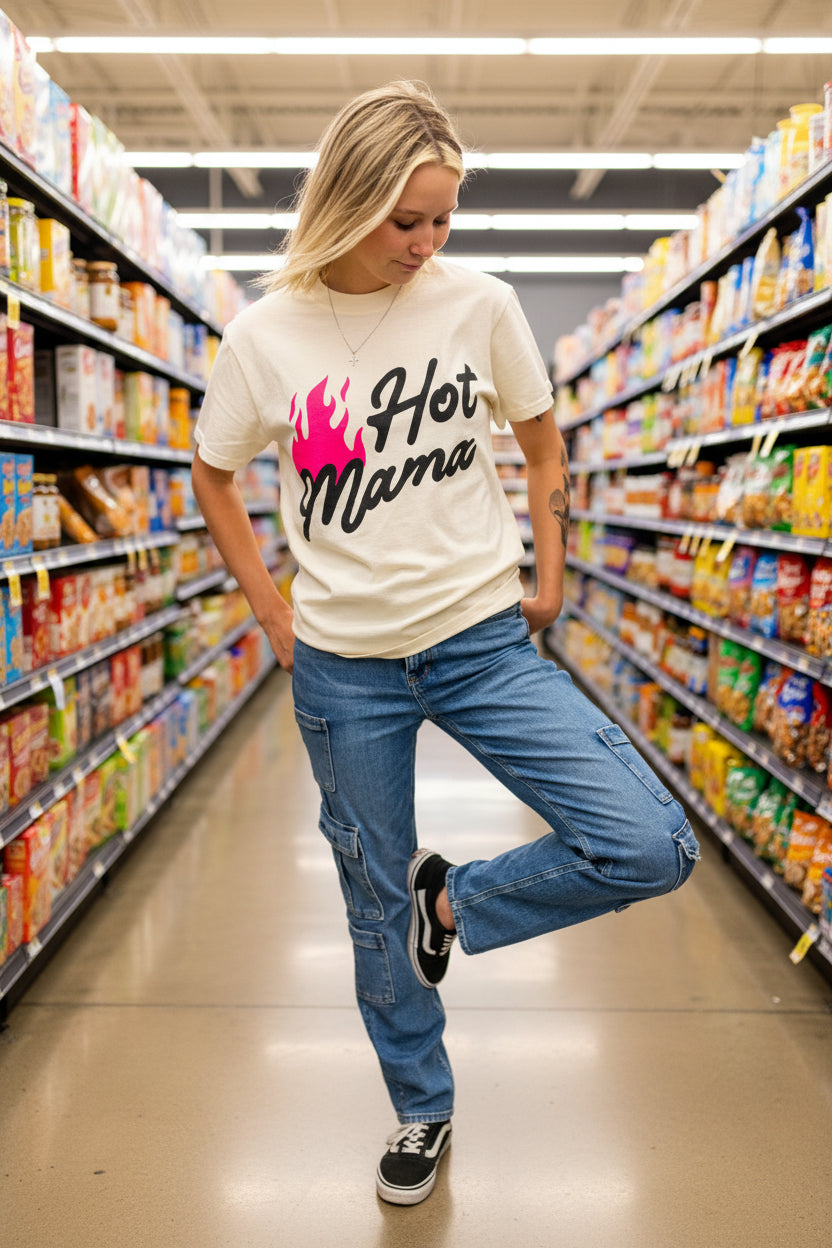 Person wearing a t-shirt with 'Hot Mama' text and graphics, standing against a gray brick wall.