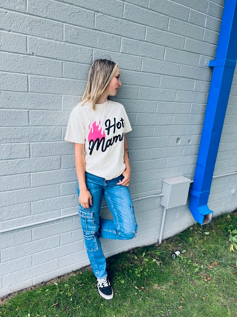 Person wearing a 'Hot Mom' t-shirt leaning against a gray brick wall.