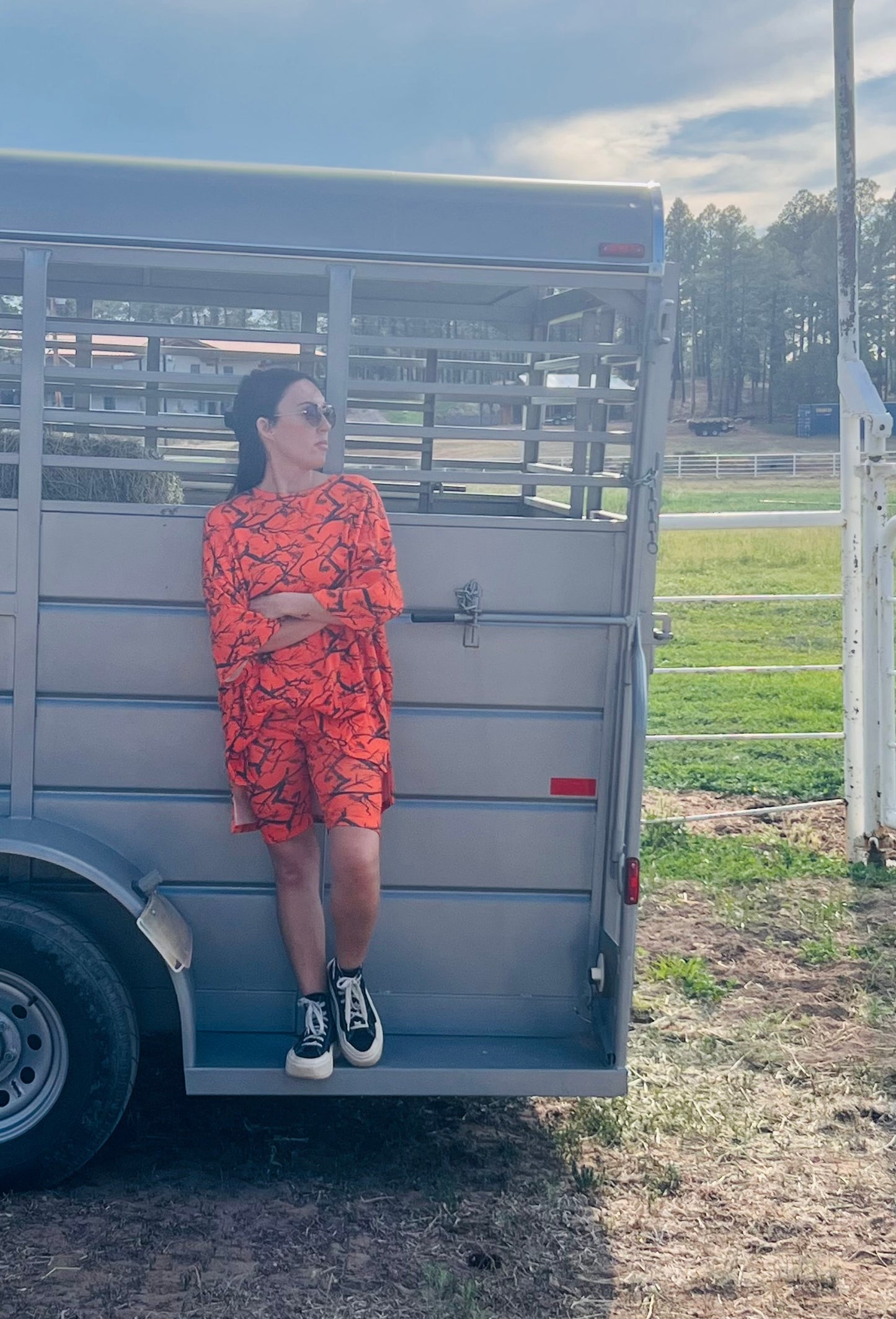 Person in an orange patterned dress standing next to a metal trailer in an outdoor setting.