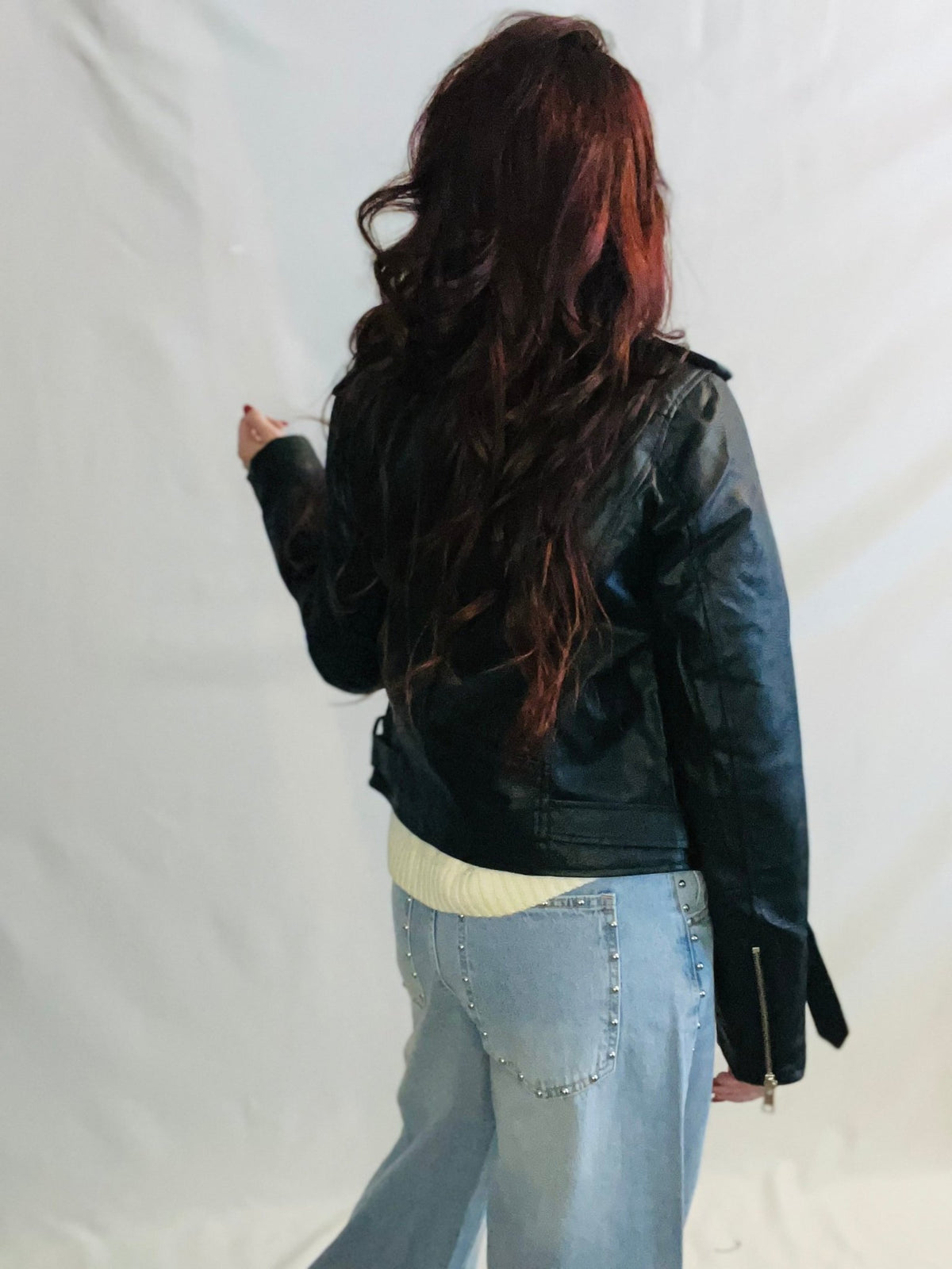 Person wearing a black leather jacket and light blue jeans against a white background