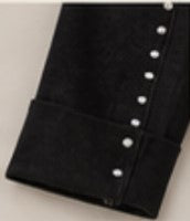 Close-up of a black hem of pants with a row of small silver studs along the edge, photographed against a light neutral background.