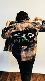 Person wearing a plaid shirt with graphic designs on the back, standing against a white wall.