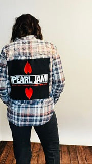 Person wearing a plaid shirt with a Pearl Jam logo on the back against a white wall.