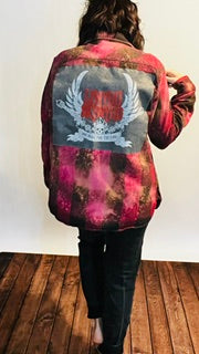Person wearing a colorful jacket with a graphic design on the back against a white wall.