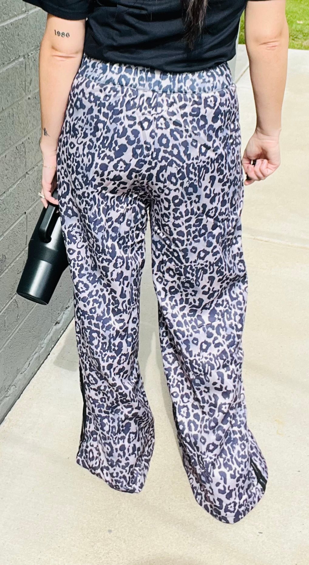 Person wearing leopard print pants and a black top, holding a black clutch.