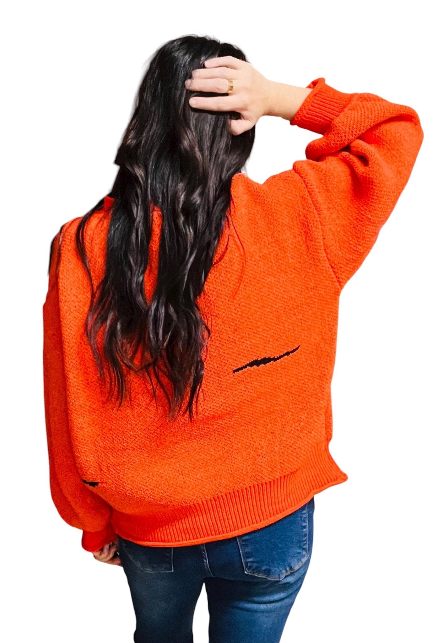 Person wearing an orange sweater with a black design on the back, standing against a white background