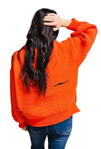 Person wearing an orange sweater with a black design on the back, standing against a white background
