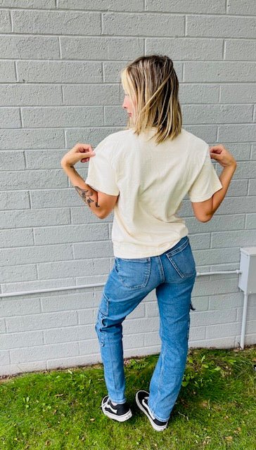 Person wearing a white t-shirt and blue jeans standing against a gray brick wall.