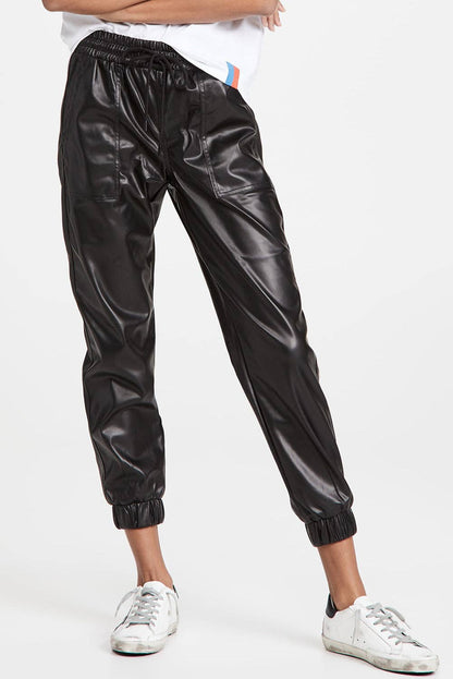 Black shiny pants worn by a person on a white background