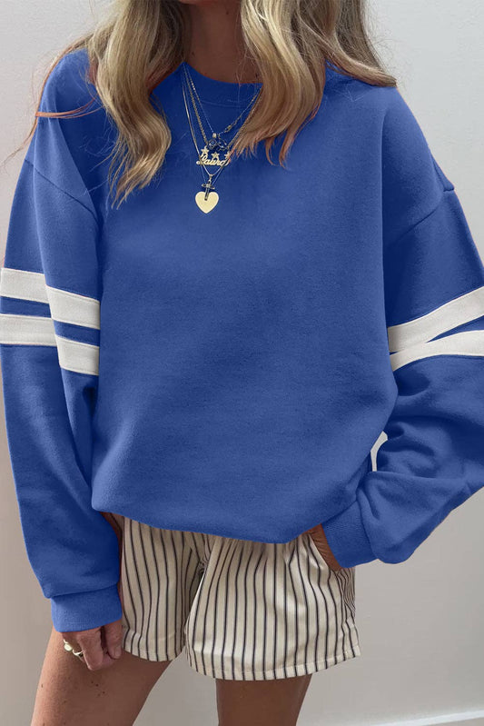 Oversized blue varsity sweatshirt with white striped sleeves and casual streetwear styling