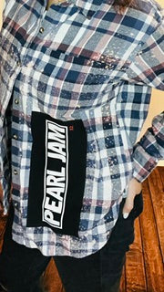 Person wearing a plaid shirt with a visible Pearl Jam band logo on a wooden floor.