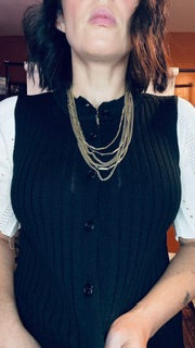 Person wearing a black dress with white sleeves and gold necklace.