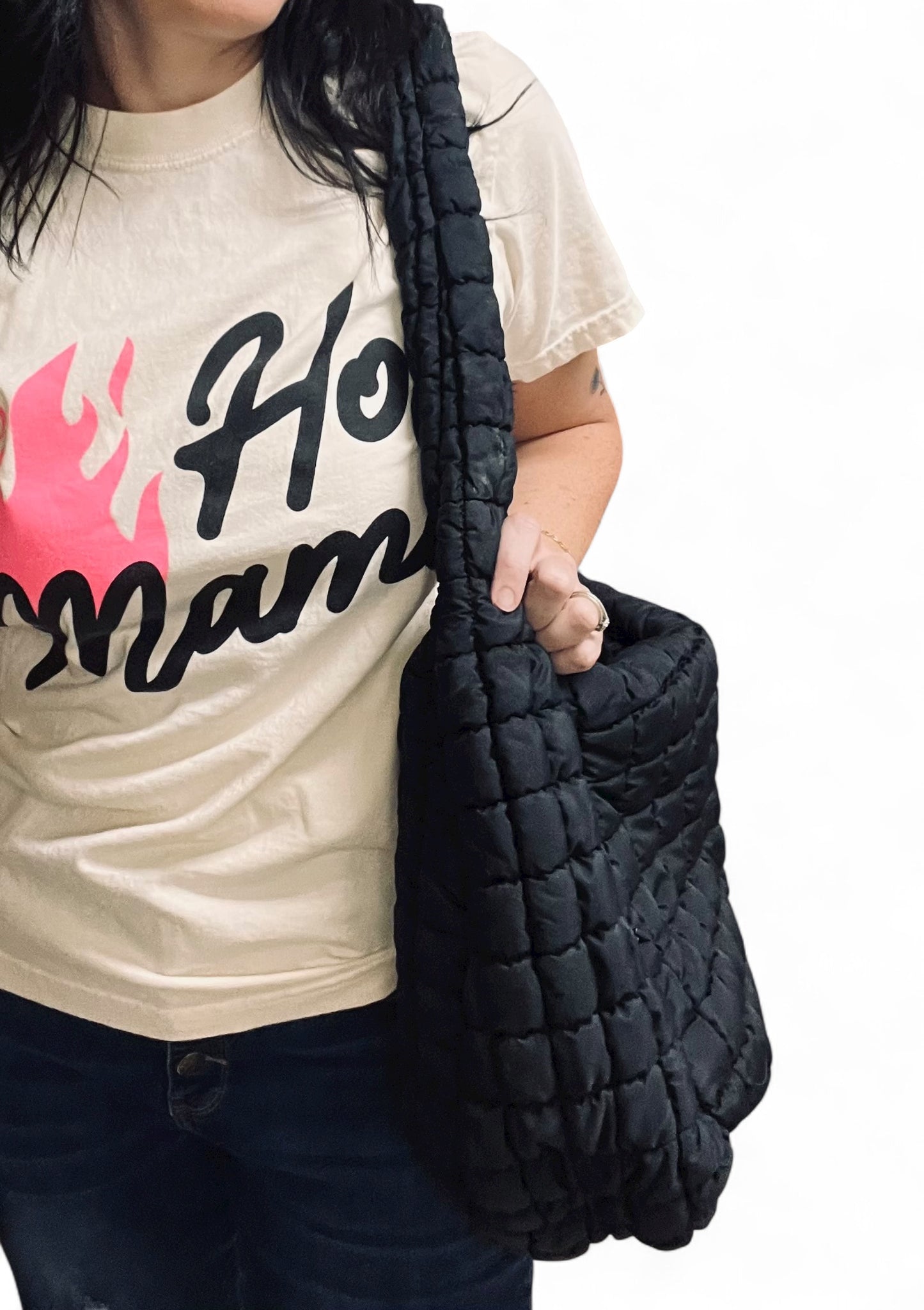 Person wearing a beige t-shirt with text and holding a black quilted bag.