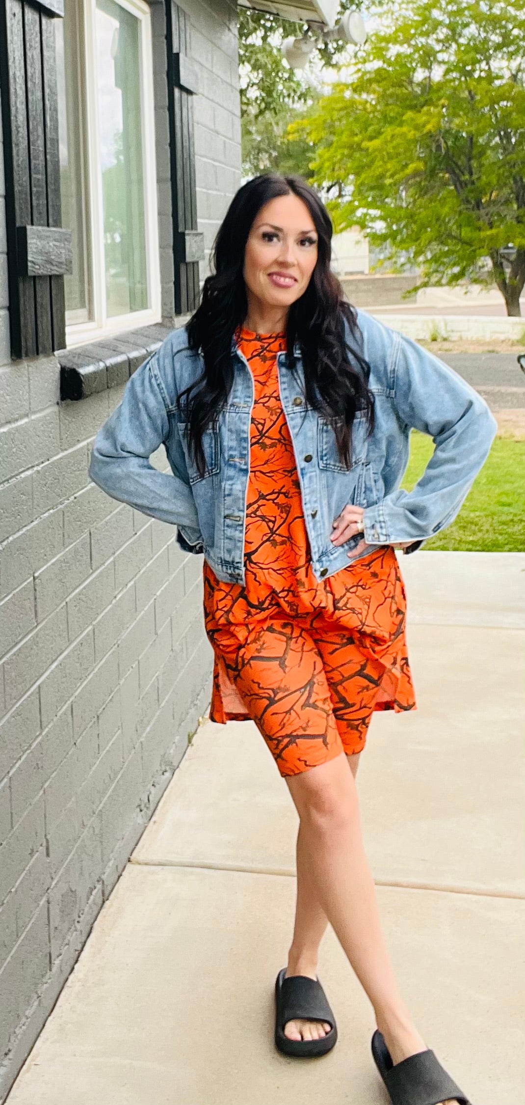 Woman wearing an orange outfit with a denim jacket standing on a sidewalk.